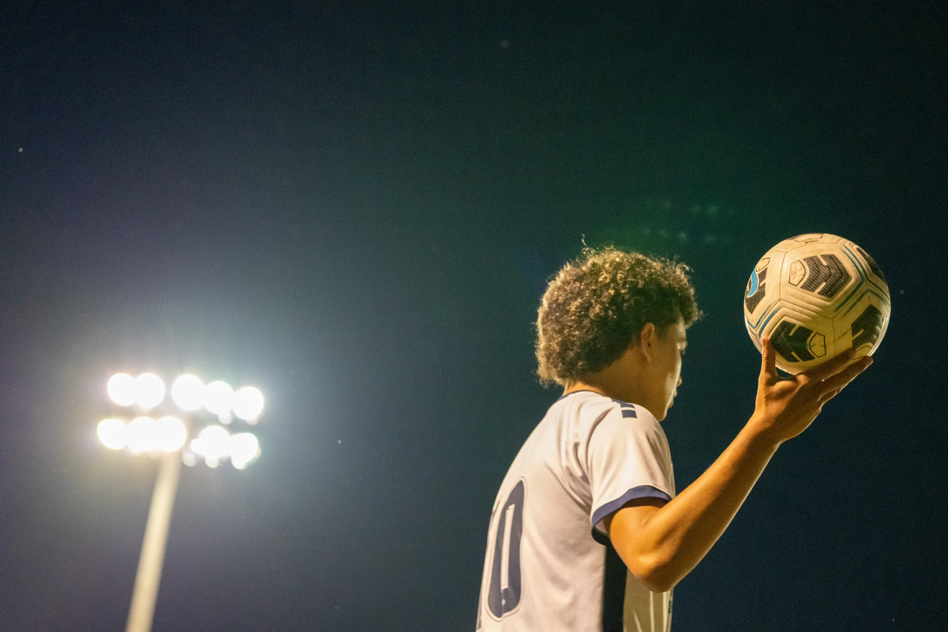 Soccer player holding the ball beneath stadium lights